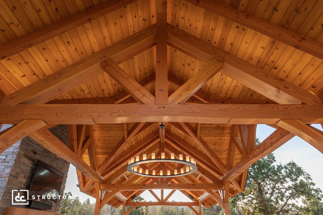 A view from below of a wooden vaulted ceiling with exposed beams and a circular modern light fixture, showcasing detailed woodwork and natural lighting.