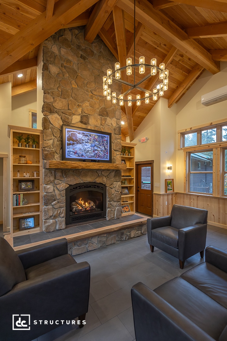 A cozy living room with a stone fireplace, built-in wood shelves, leather armchairs, TV above the mantle, and modern chandelier.