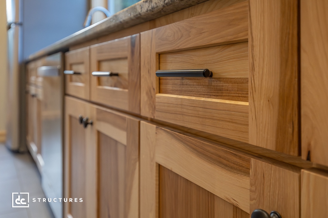Close-up view of light wood kitchen cabinets with modern black handles, under a granite countertop.