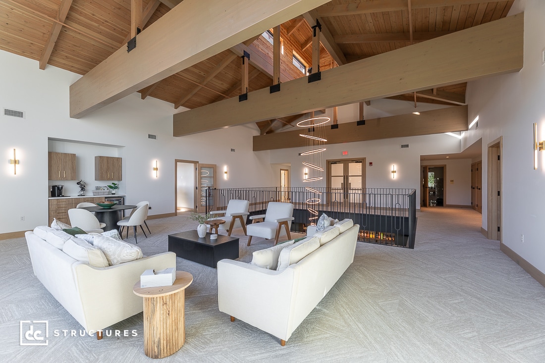 Spacious modern living room with high vaulted wood ceilings, white sofas, armchairs, black coffee table, spiral chandelier.