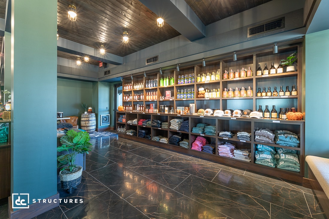 A modern retail shop interior with shelves of bottles, hats, merchandise, and folded shirts. Dark wood accents and glossy marbled floors.