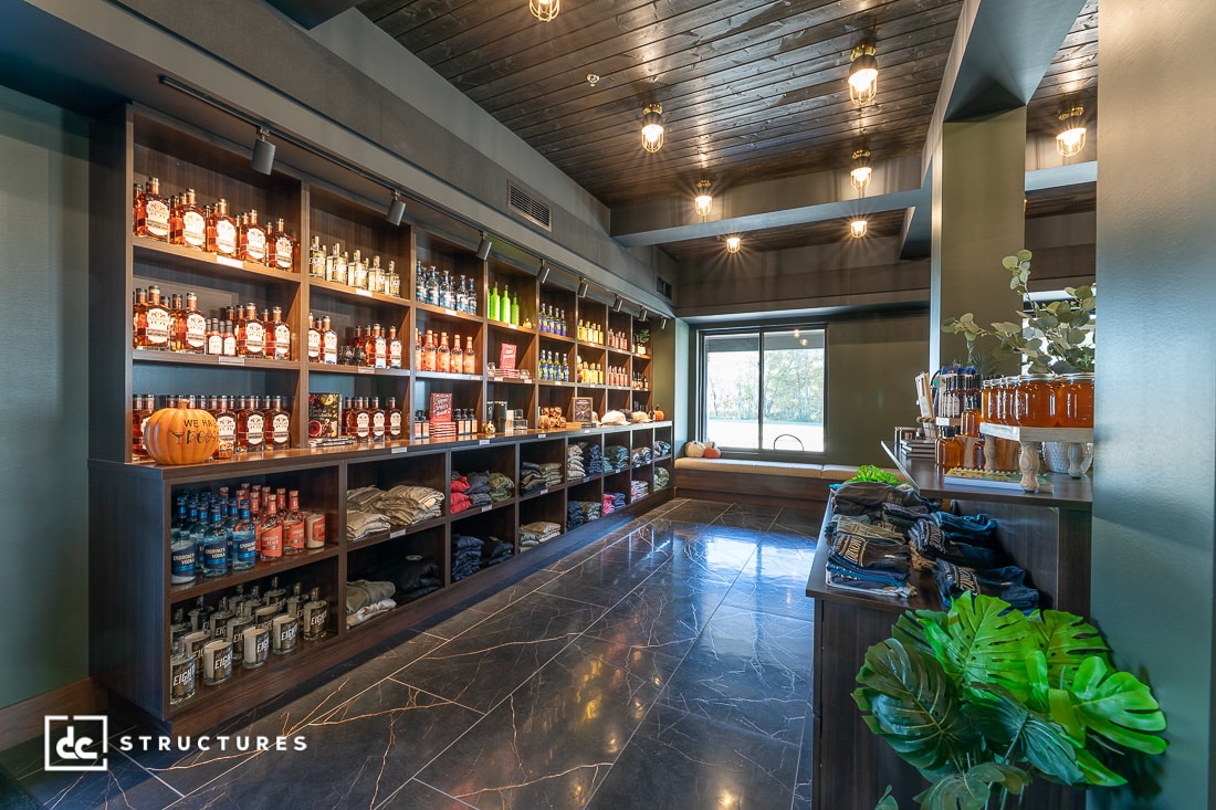 A modern liquor store with dark wood shelves displaying bottles, clothing, and souvenirs. Shiny black tile floor and green walls.
