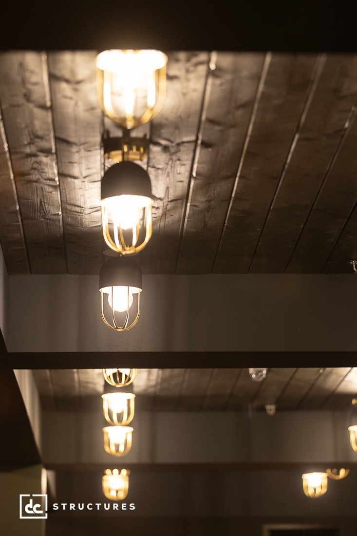 Rows of warm, modern pendant lights with wire cages hang from a dark wooden ceiling, creating a cozy and stylish atmosphere.