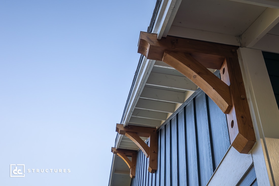 Close-up view of wooden brackets supporting the overhang of a building roof, with blue vertical siding and a clear sky in the background.