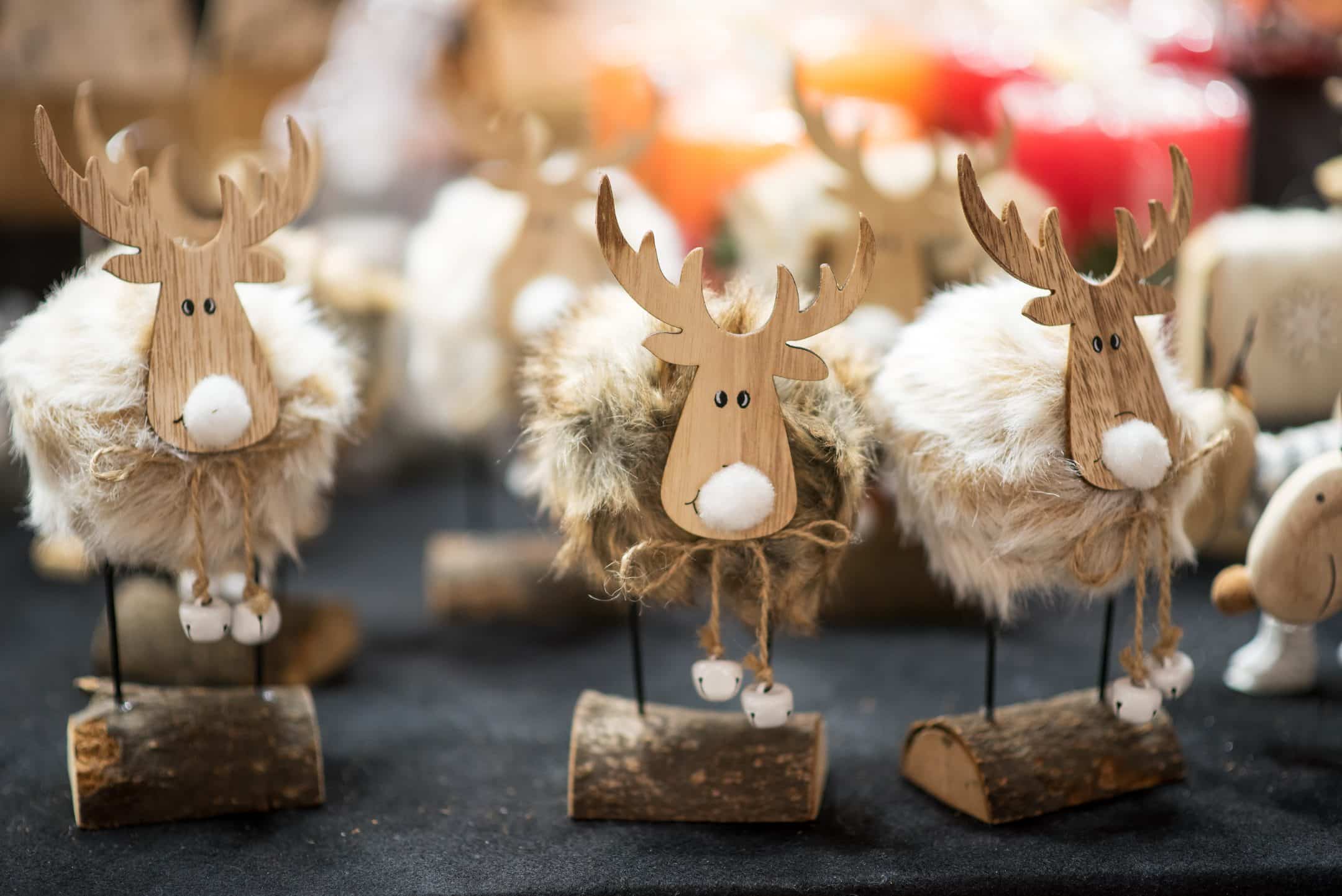 Three handmade reindeer figures with wooden faces, antlers, and fluffy bodies sit on log bases on a black surface.