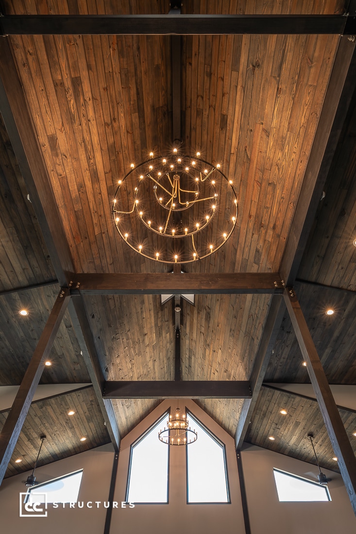 A wooden cathedral-style ceiling with exposed beams, two round chandeliers, and large triangular windows letting in natural light.