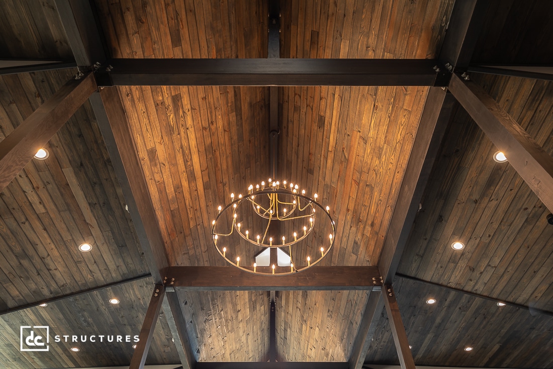 Wood-paneled vaulted ceiling featuring a large circular chandelier with multiple lit bulbs. Dark wooden beams and recessed lights are visible.