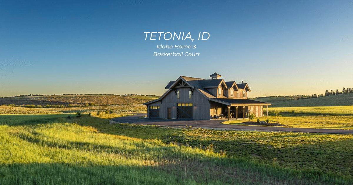 https://dcstructures.com/projects/idaho-home-basketball-court/ A large modern barn-style home sits on a green field under a clear blue sky in Tetonia, Idaho. Sunlight casts long shadows across the grass.