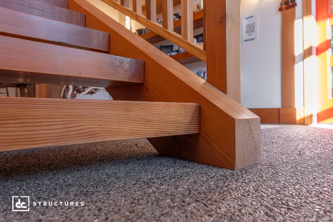 Close-up view of a wooden staircase with exposed beams, set on a textured carpeted floor in a well-lit interior space.