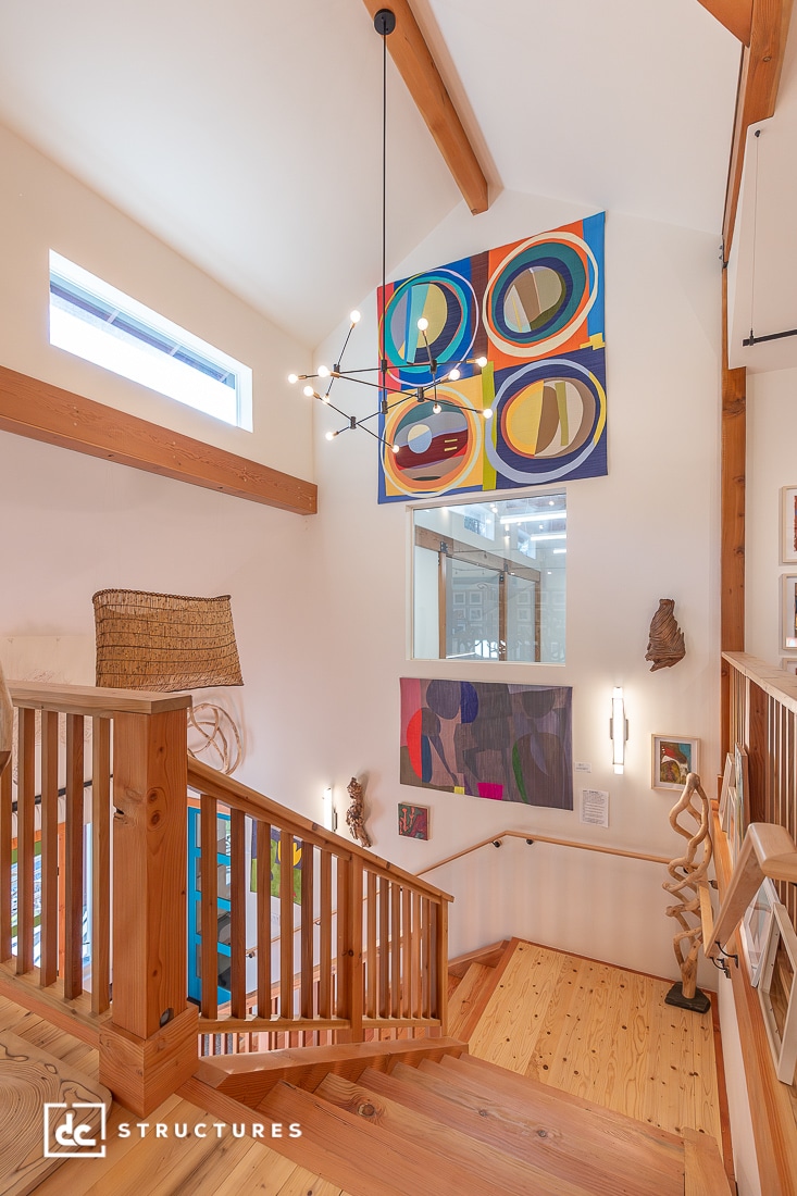 Modern wooden staircase with light wood railings, colorful abstract art on white walls, large windows, and contemporary decor.