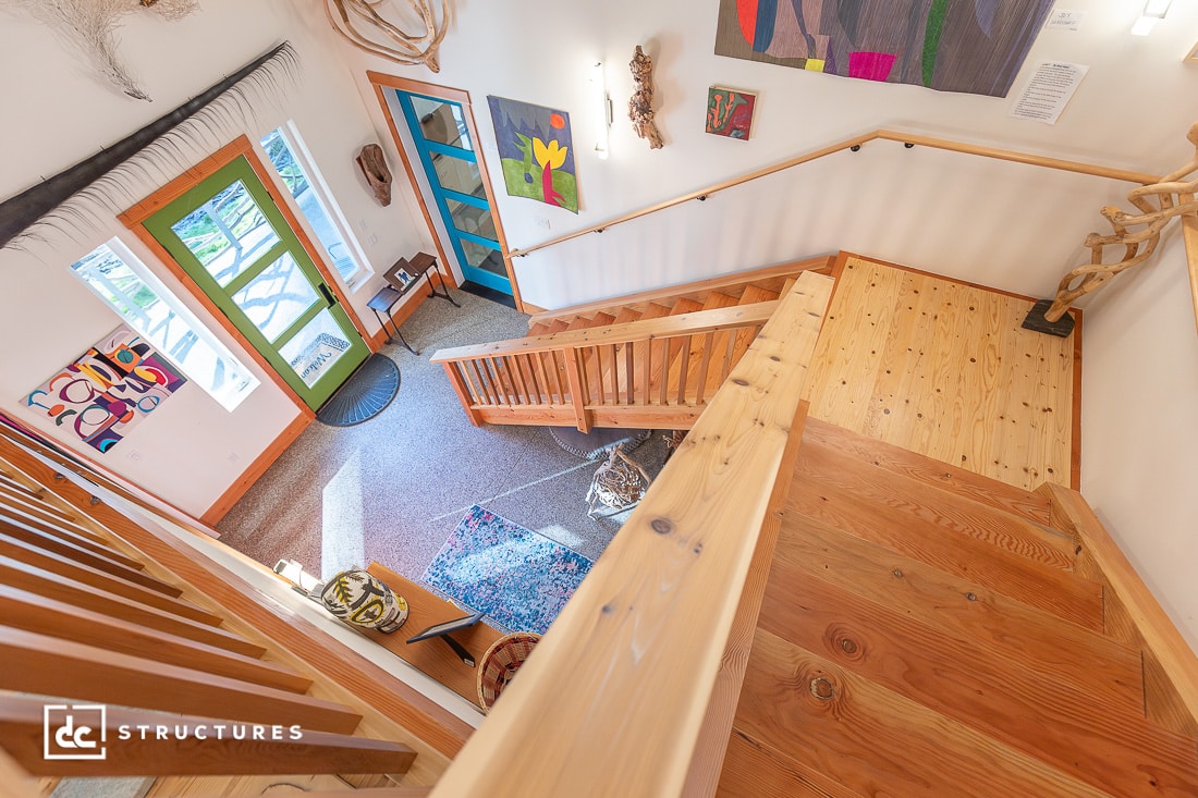 An interior view looking down a wooden staircase with art on the walls and a green door.