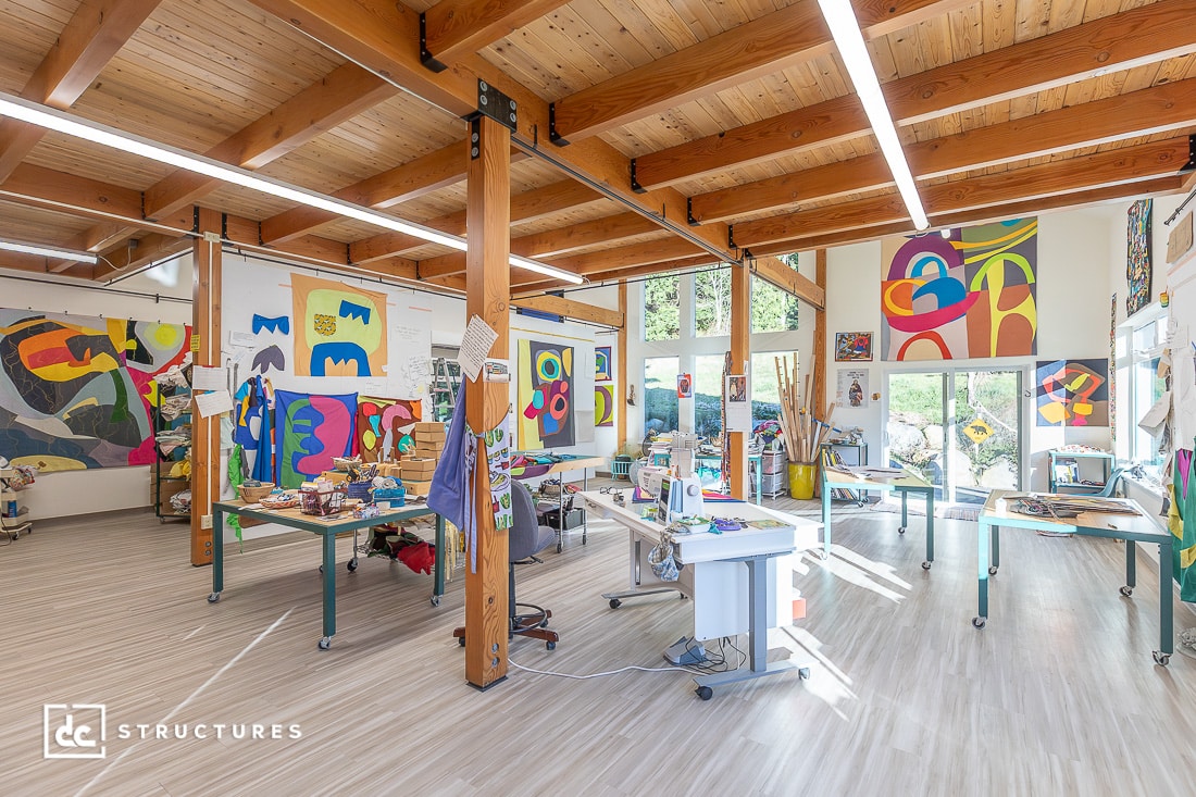 A bright, open art studio with colorful artwork on the walls, worktables, and natural light streaming in.
