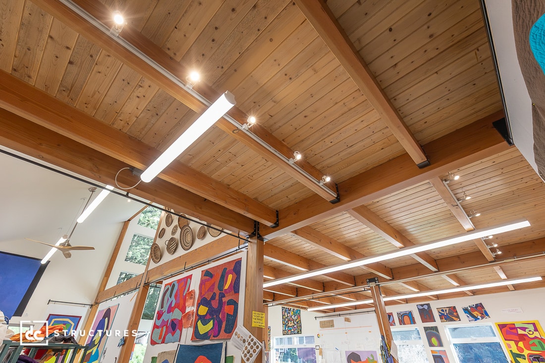 Modern interior featuring a wood-paneled ceiling, exposed beams, track lighting, and vibrant artwork on the walls.