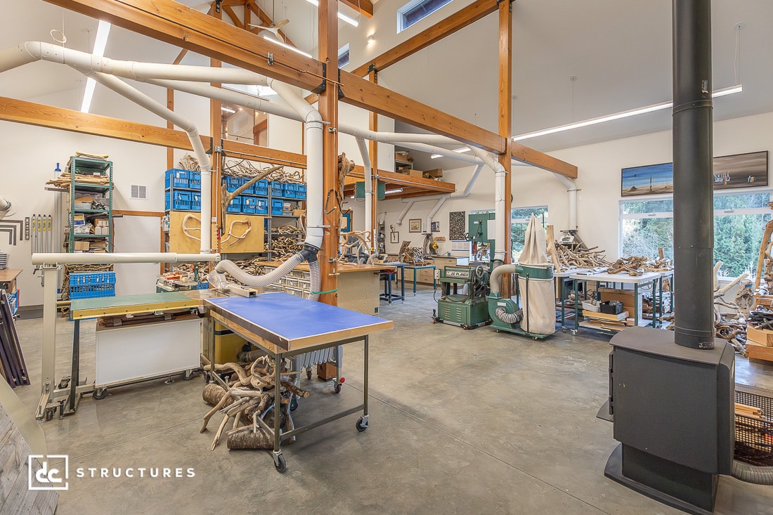 A spacious workshop with wooden beams, industrial equipment, and piles of driftwood.
