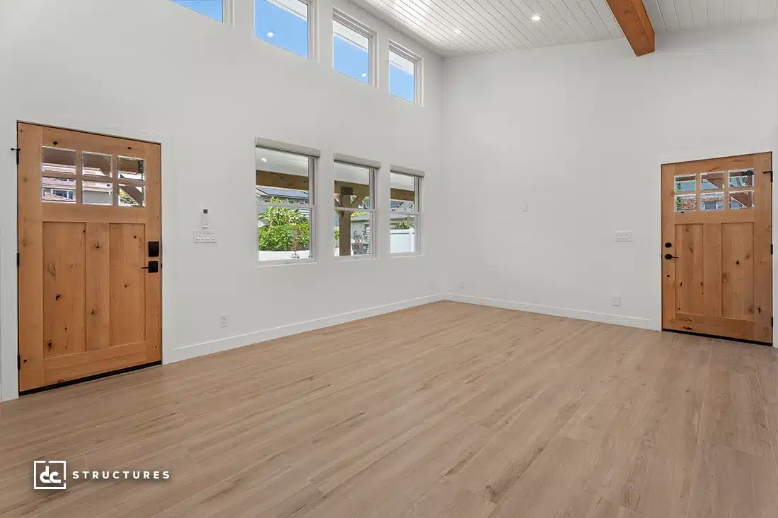 A spacious, empty room with light wood floors, white walls, and a high ceiling. Wooden doors with glass panes face each other.