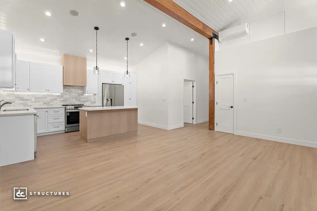 A spacious, modern open-concept kitchen and living area with light wood flooring, white cabinets, center island, and vaulted ceilings.