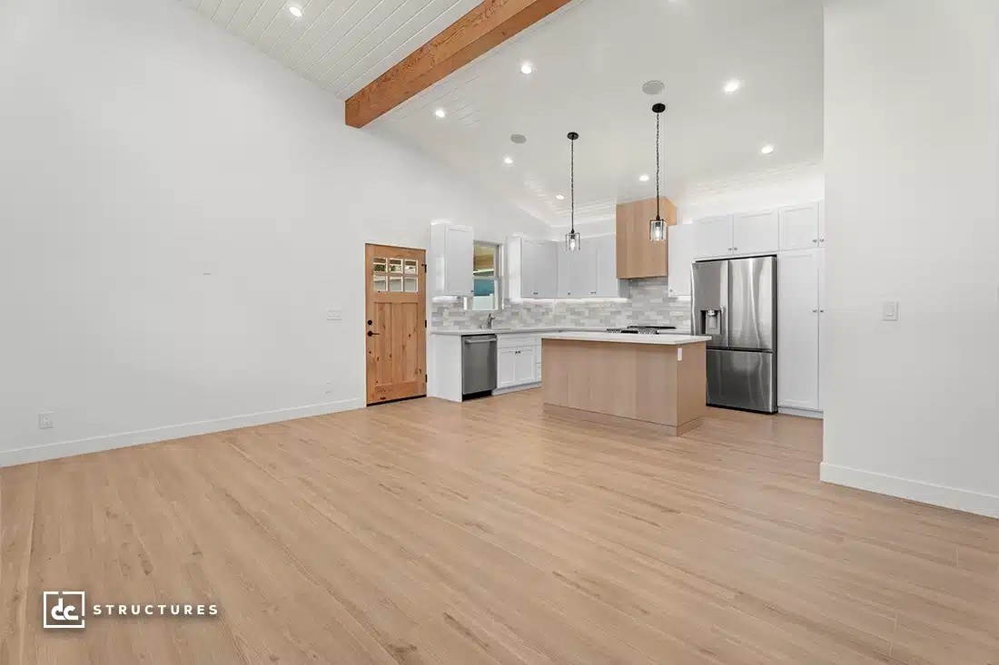 A modern, open-concept kitchen with white cabinets, stainless steel appliances, a wooden island, and light wood flooring.