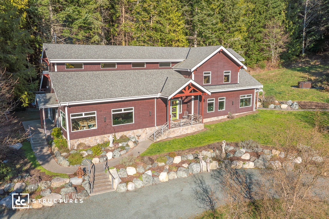An aerial view of a large, two-story dark red home nestled amongst tall green trees with a gray roof and numerous windows.