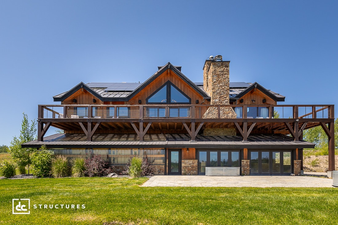 A two-story mountain-style house with a stone chimney, solar panels, and a large wooden deck designed for outdoor living.